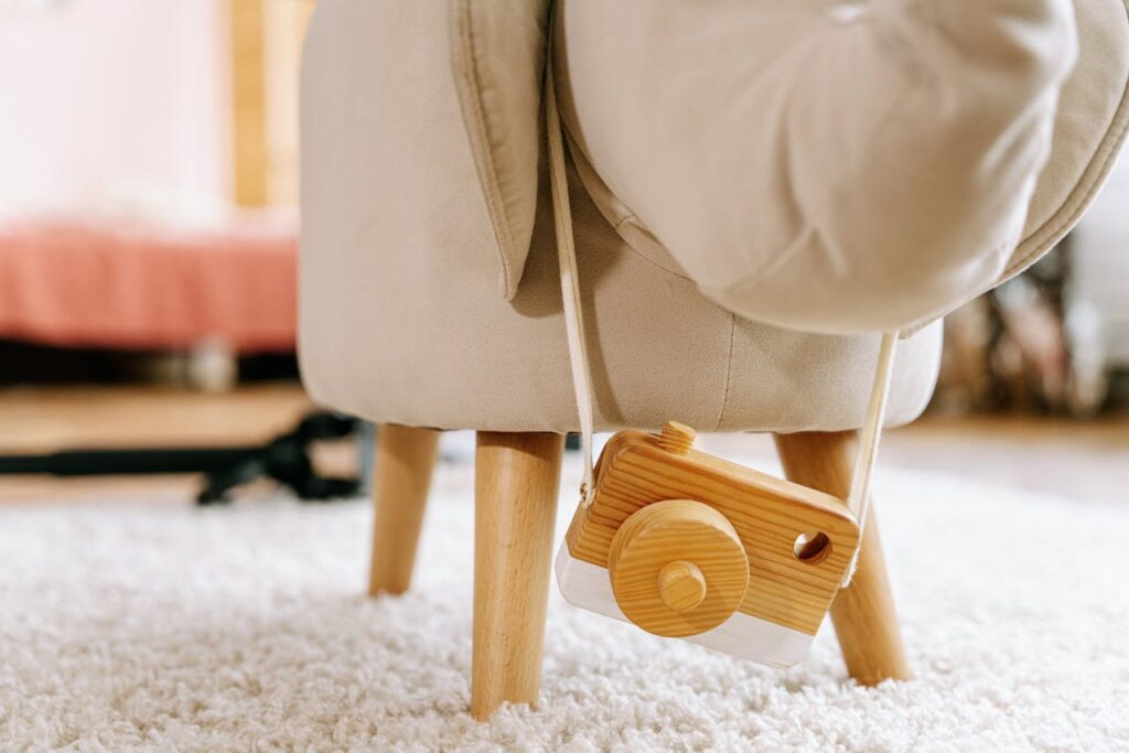 Close-up of a wooden toy camera hanging from a child's plush chair in a cozy room.